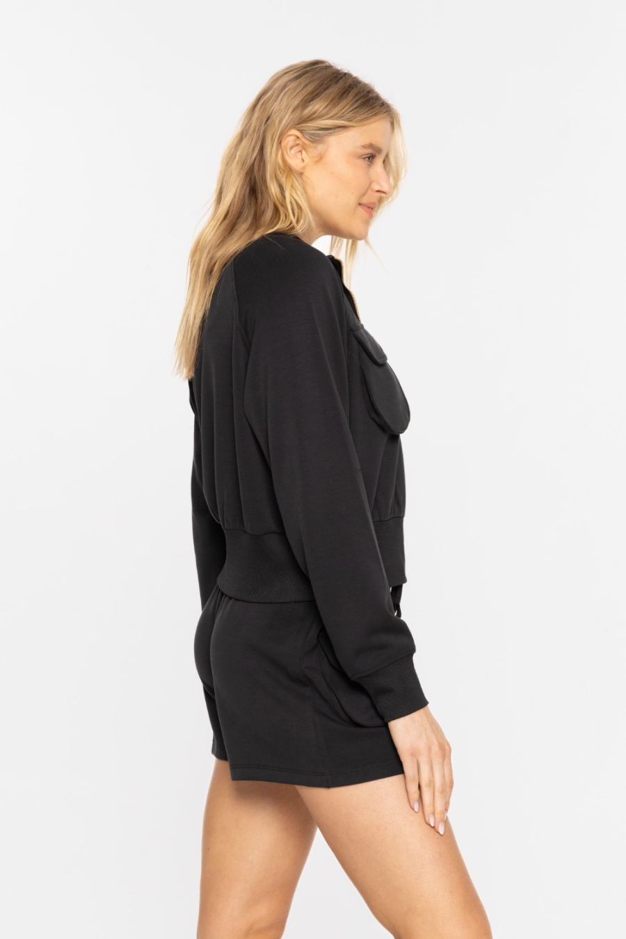 Close up side view of the cropped mock neck zip up jacket in the color black 