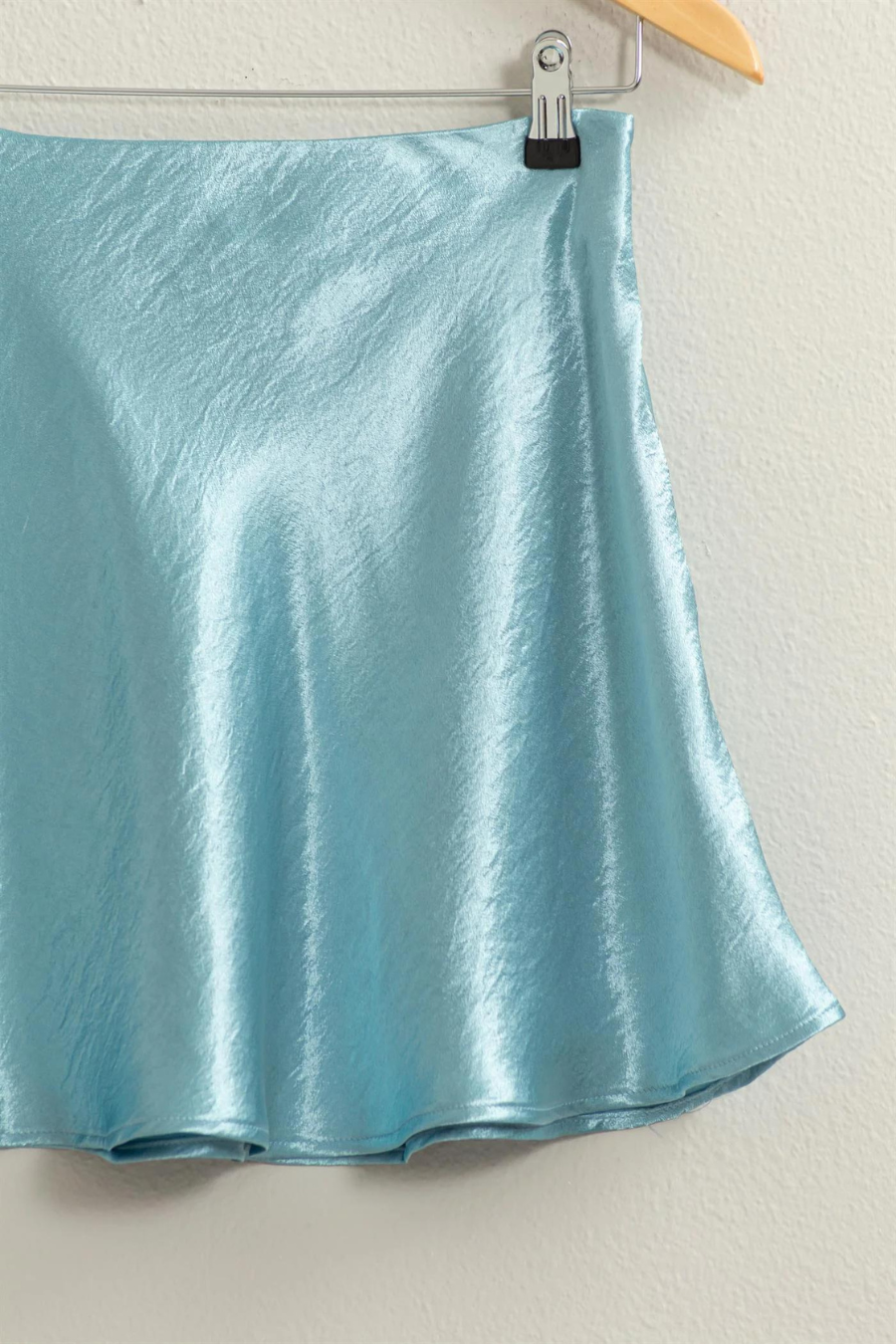 close up of Teddi satin mini skirt in the color aqua, hanging on a hanger