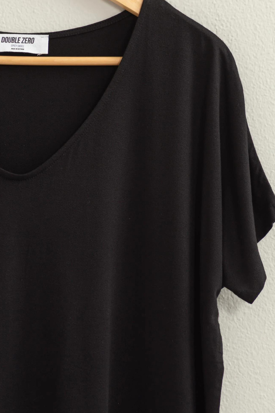 close up front view of the andi tee in the color black, hanging on a wooden hanger 