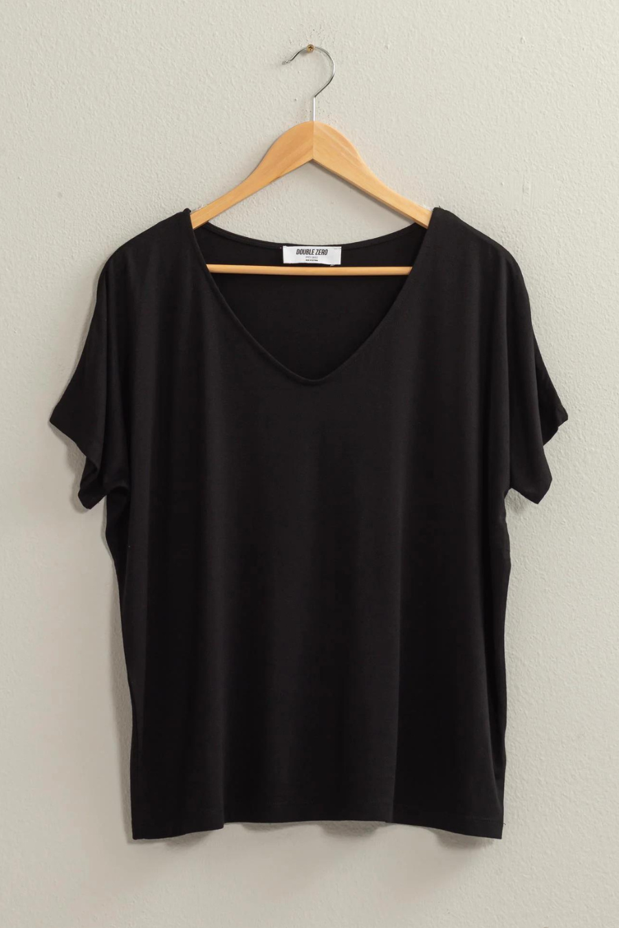 full length front view of the andi tee in the color black, hanging on a wooden hanger 