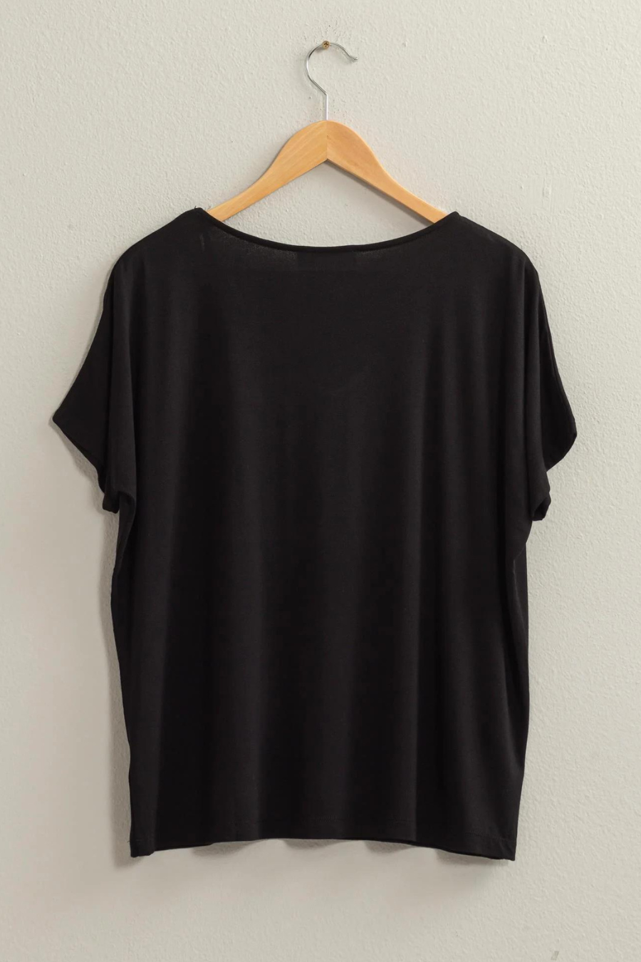 full length back view of the andi tee in the color black, hanging on a wooden hanger 