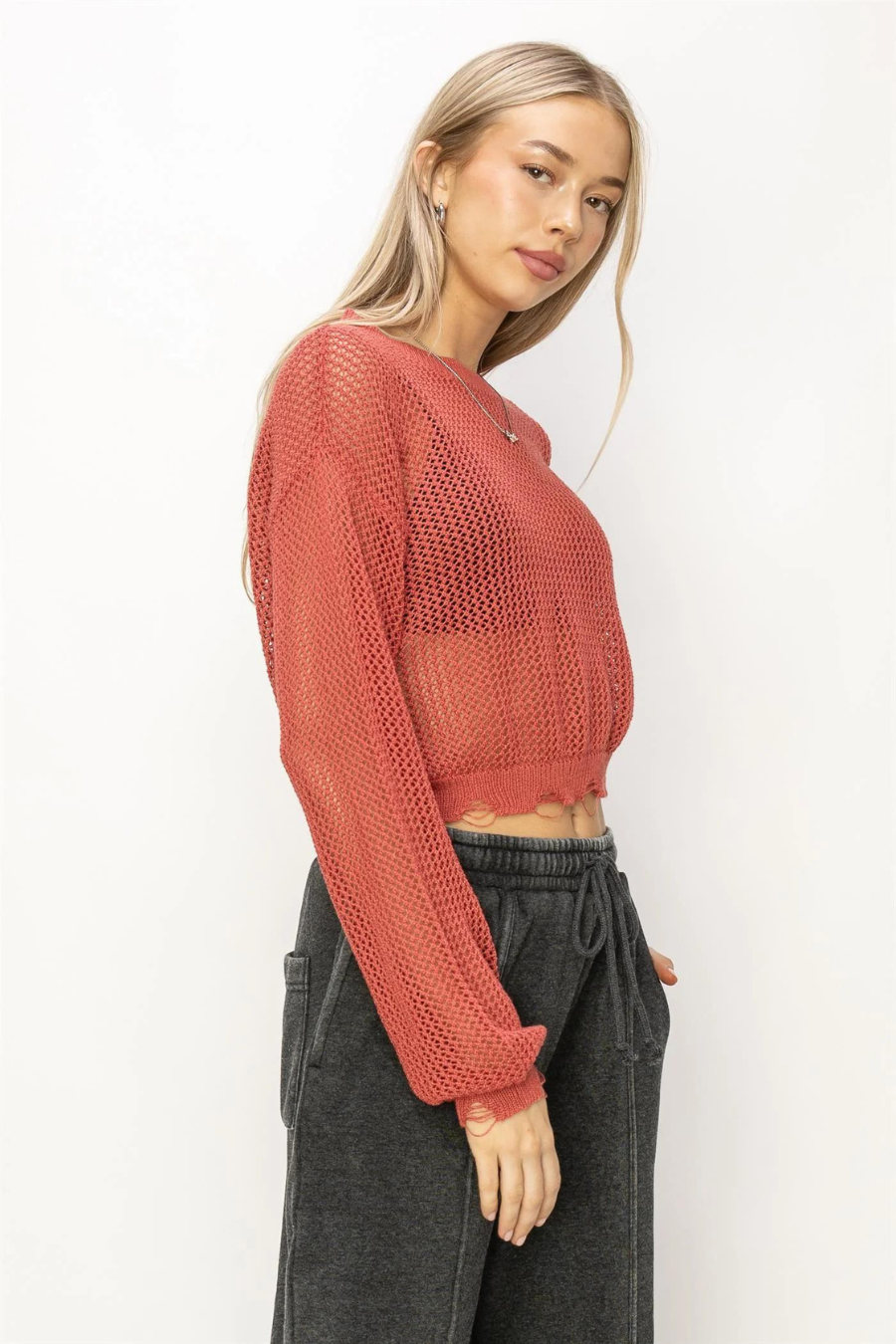 side front view of junie distressed knit sweater in the color rust. model is wearing it with black sweat pants 