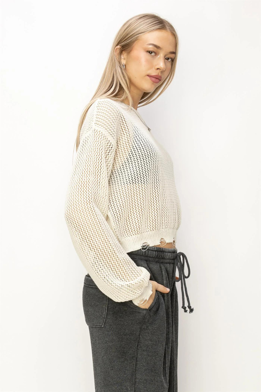 side front view of the junie distressed knit sweater in the color ivory, model is wearing it with charcoal sweatpants 