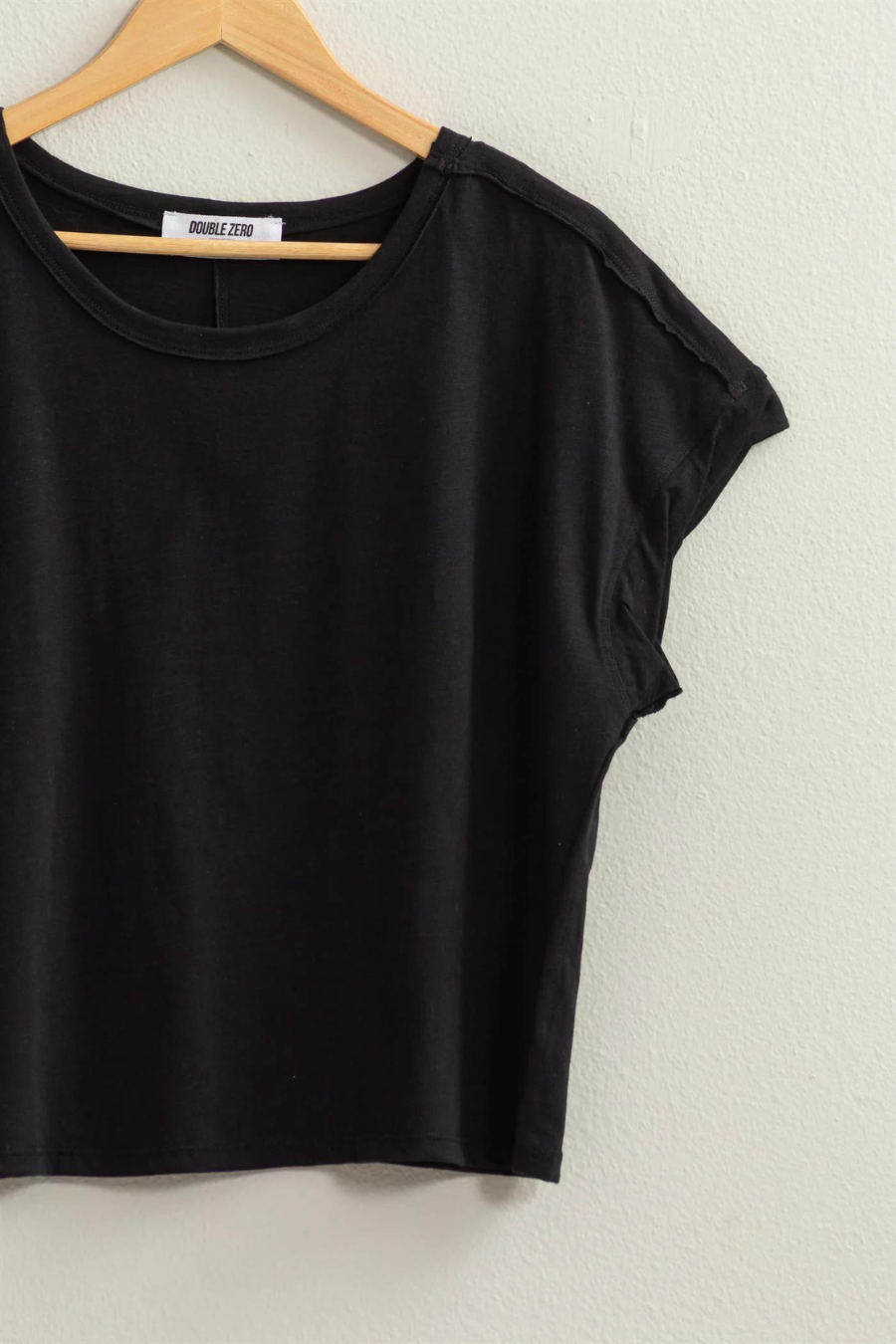 close up detail shot of Hunter raw edge tee in the color black,  shirt if hanging on a wooden hanger