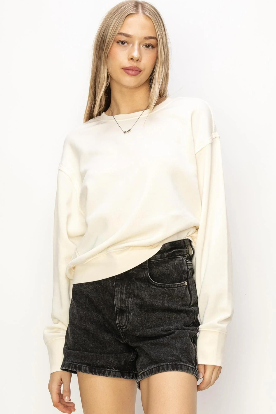 close up front view of maxi pullover sweatshirt in the color ivory, model is wearing it with black denim shorts 