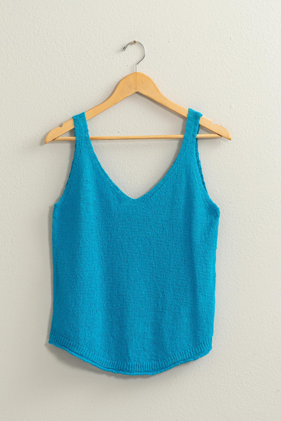 full length shot of blue knit top hanging on a wooden hanger 