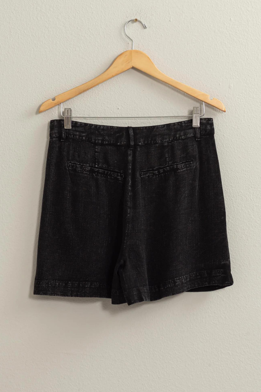 full length back shot of black washed linen shorts on a wooden hanger