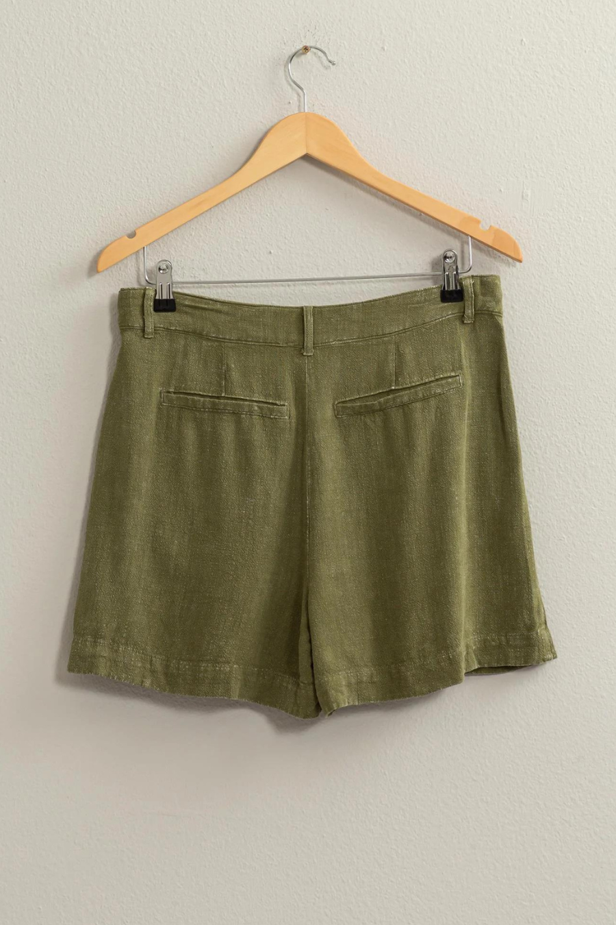 back view of olive green linen shorts on wooden hanger