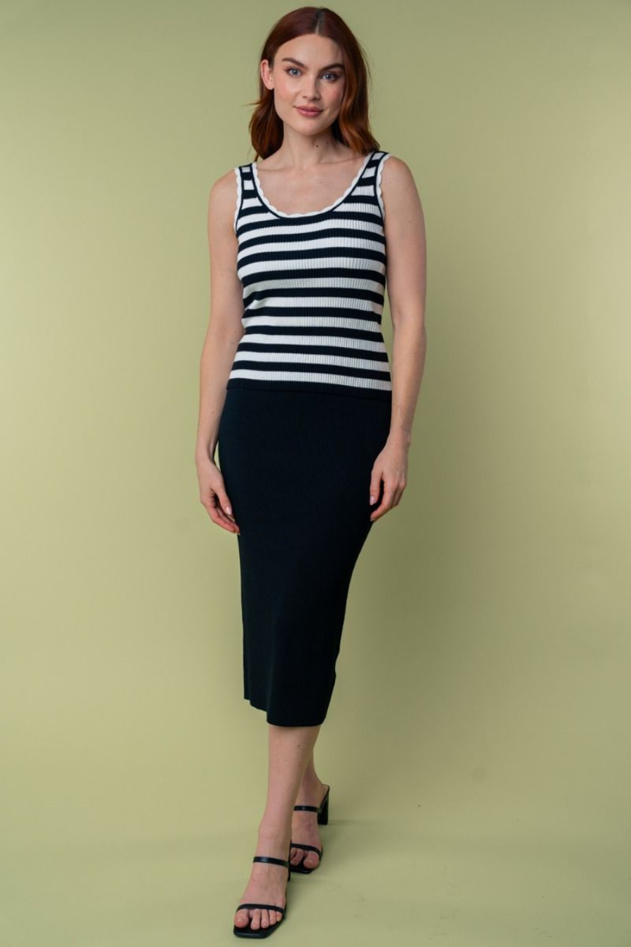 full length front view of Julianna high waisted knit midi skirt in the color black. model is wearing with a black and white striped tank top and heels