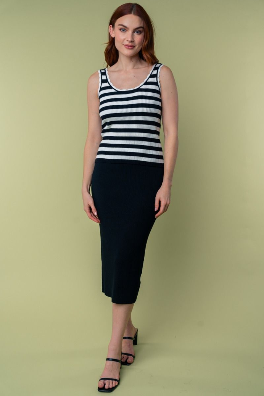 full length front view of Julianna high waisted knit midi skirt in the color black. model is wearing with a black and white striped tank top and heels 