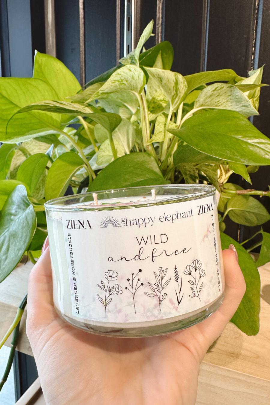 close up of wild and free candle in front of a plant 