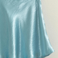 close up of Teddi satin mini skirt in the color aqua, hanging on a hanger 