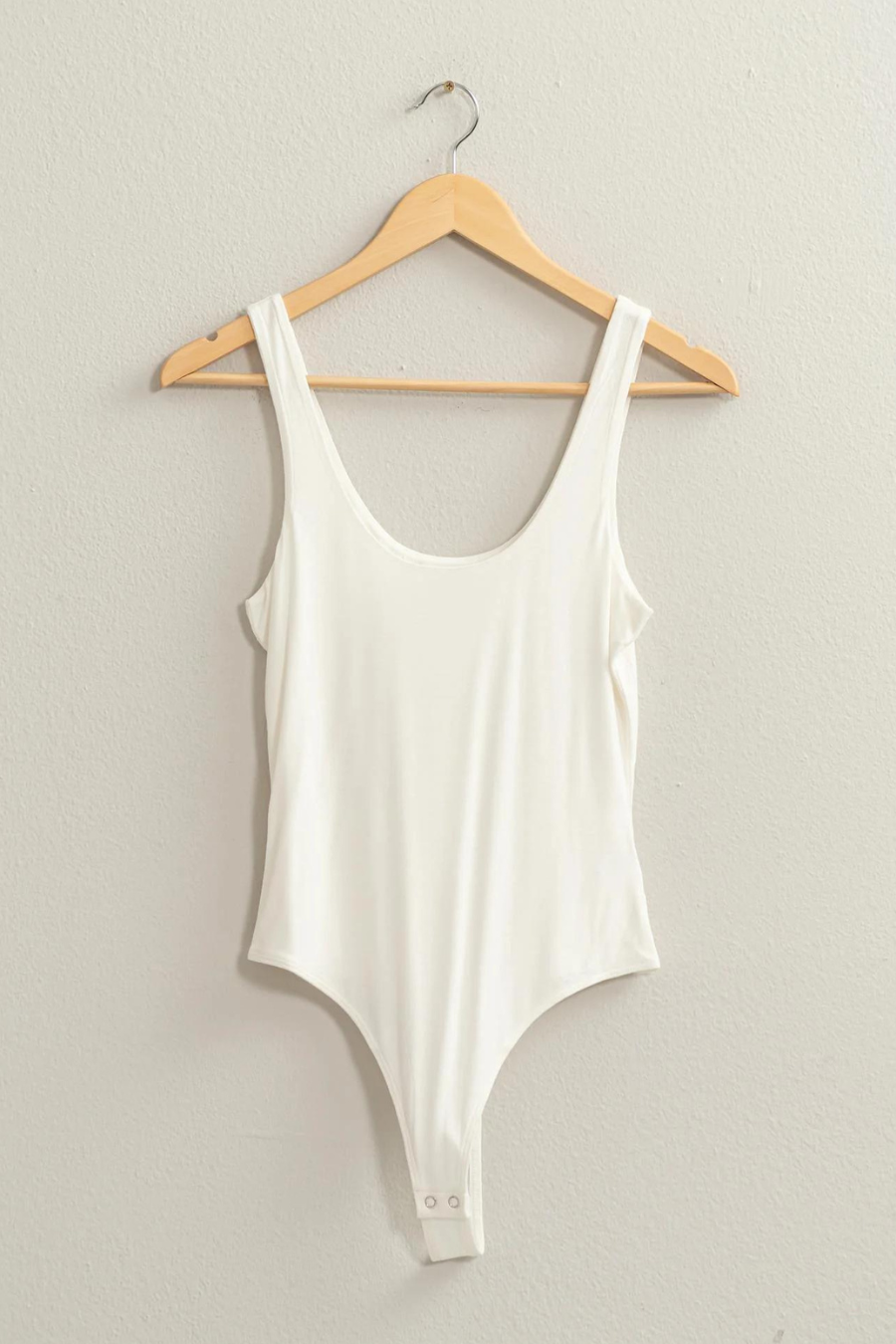 full length view of the brinkley body suit, shown in the color ivory, hanging on a hanger 