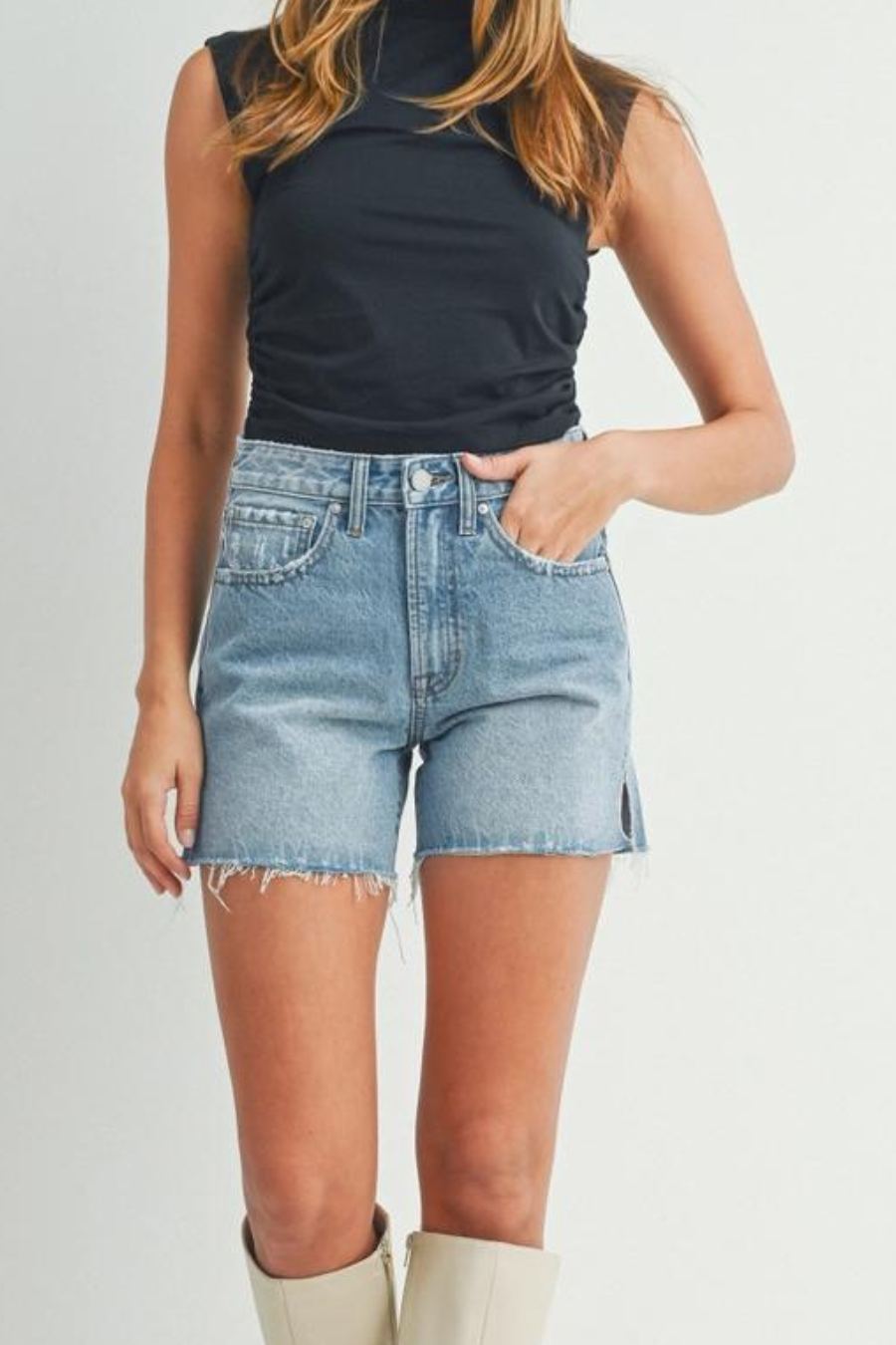 close up of girl wearing black turtleneck tank with denim shorts with slits on the sides and cream boots 
