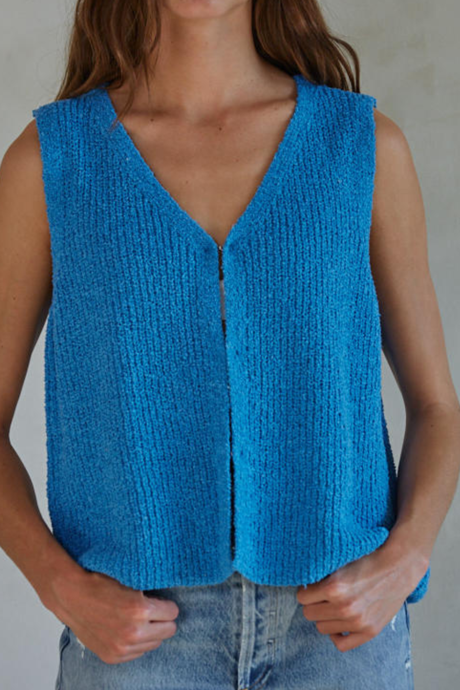 girl wearing knit blue sleeveless sweater top with hook and eye closure. she is wearing it with jeans