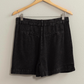 full length back shot of black washed linen shorts on a wooden hanger 