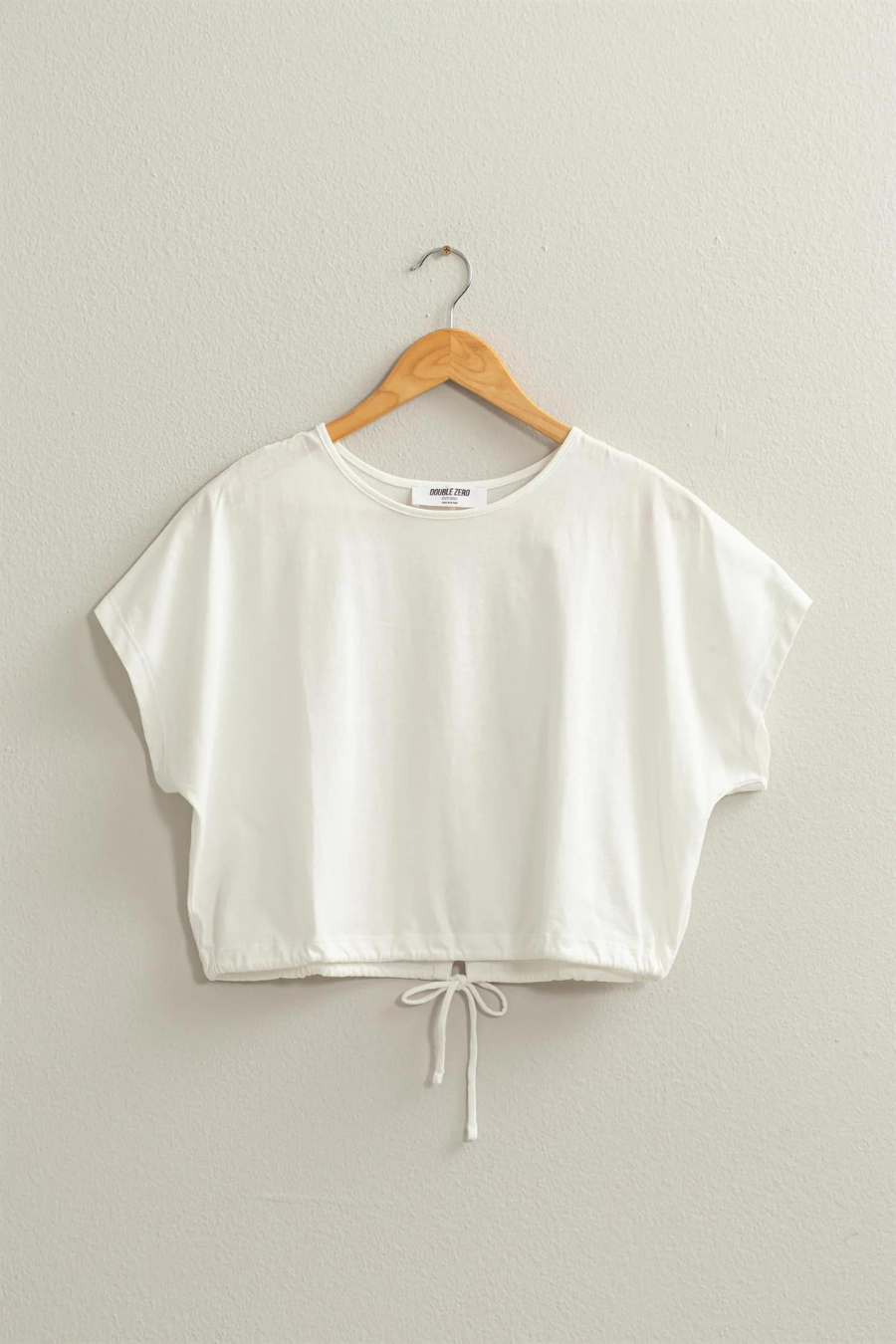 full front view of Dakota drawstring hem crop top in the color ivory, hanging on a hanger 