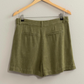 back view of olive green linen shorts on wooden hanger 
