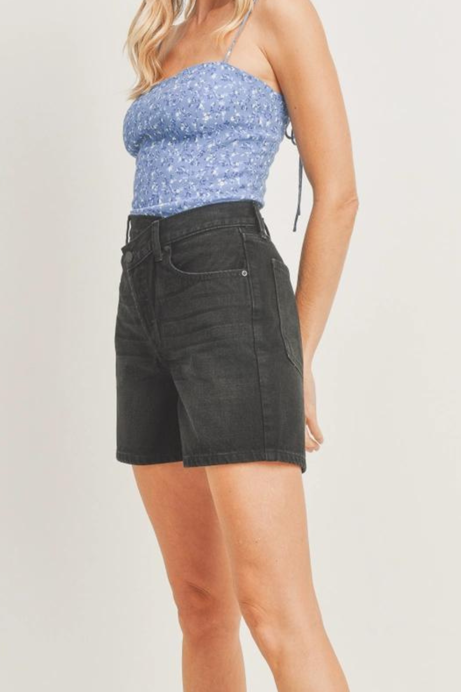 side view of girl wearing blue top with flowers on it and black denim shorts 
