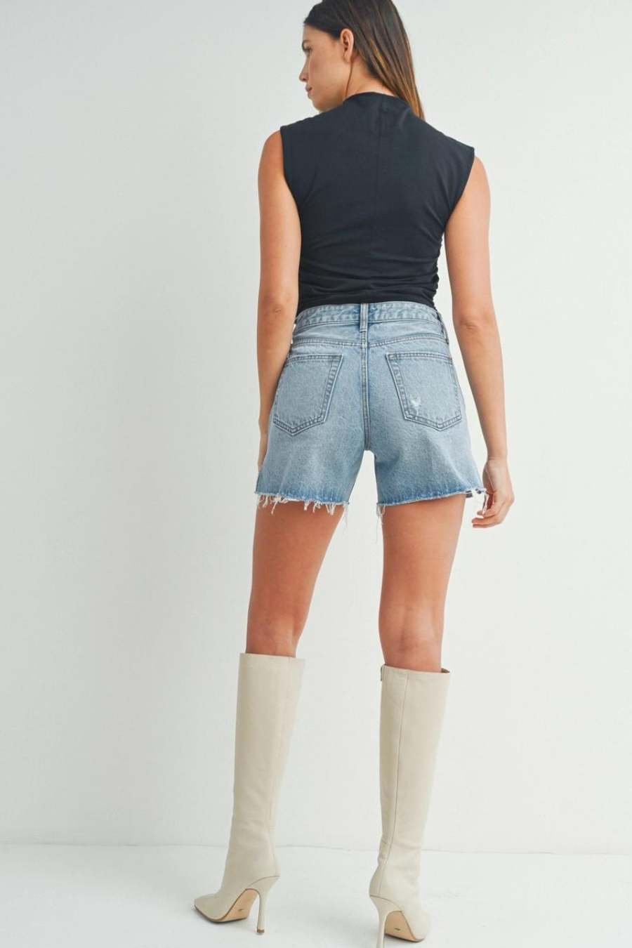 back shot of girl wearing black tank top and denim shorts paired with white boots 