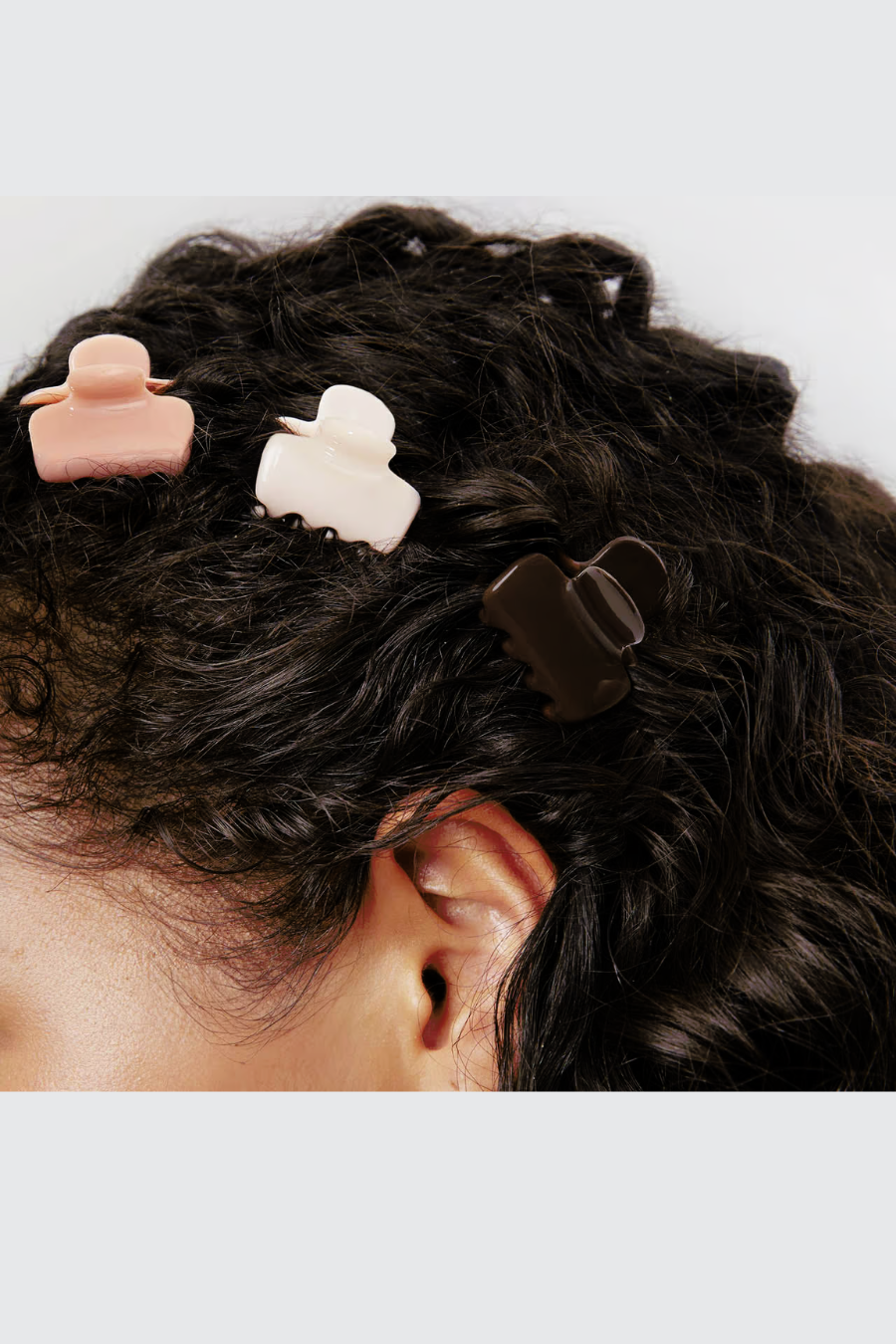 girl with curly hair using blush, white, and cocoa mini claw clips to hold her hair back 