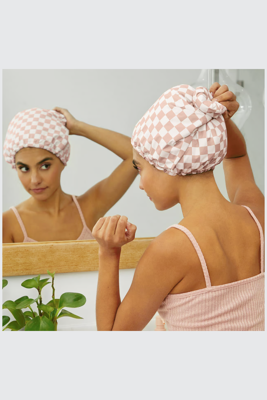 girl lookin in mirror while wearing her blush checkered shower cap