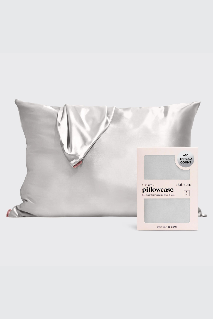 silver satin pillowcase standing upright with a pillowcase draped over it and another pillowcase in front of it in its packaging 