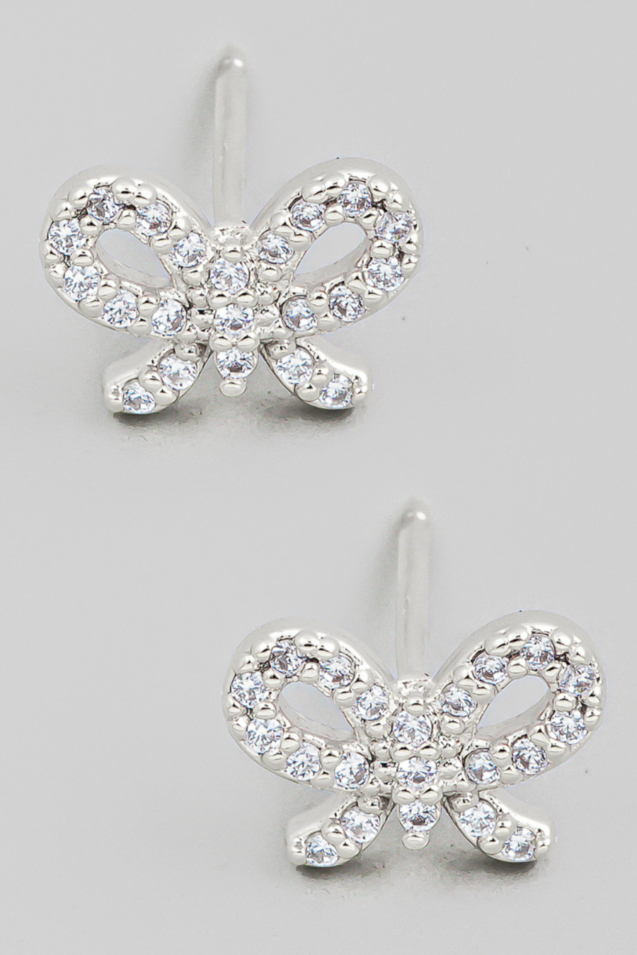 close up view of lilibet rhinestone bow stud earrings on a flat lay in silver 