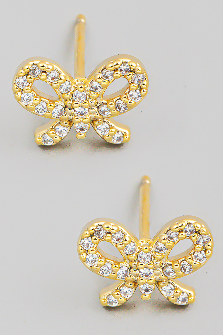 close up view of lilibet rhinestone bow stud earrings on a flat lay in gold