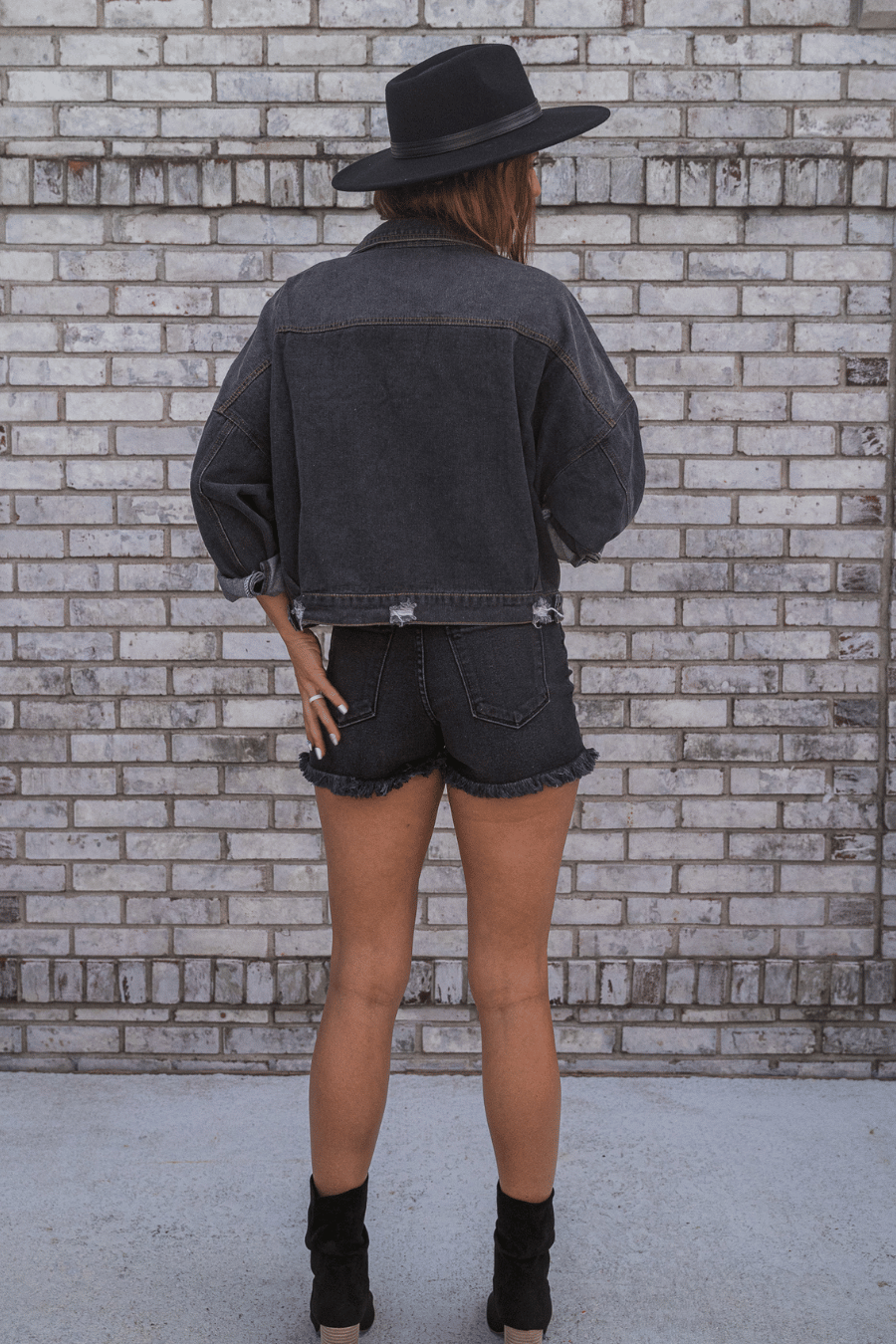 back of black denim shorts against a white brick background